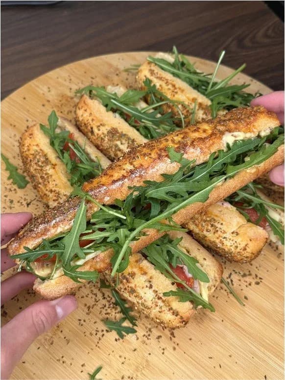 Pains maison façon Subway garnis de roquette, sur une planche en bois